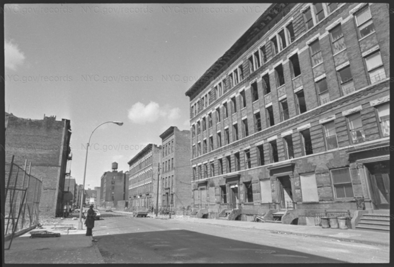 Street level view of 5-and 6-story abandoned buildings slated for demolition with a man standing on the street.